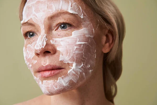 Piegowata kobieta z maską do leczenia skóry odwracając wzrok podczas pozowania — Zdjęcie stockowe