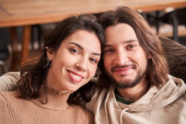 Kanepede oturmuş kameraya bakan çiftler.