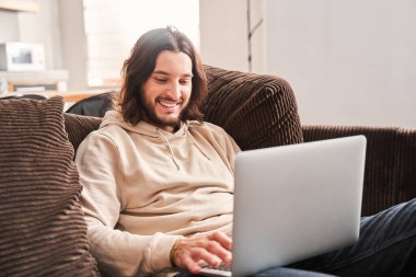 Adam gülümsüyor ve odada otururken laptop ekranına bakıyor.