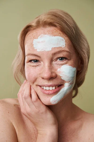 Половина гола жінка торкається щоки, маючи глиняну маску на обличчі, насолоджуючись м'якістю — стокове фото