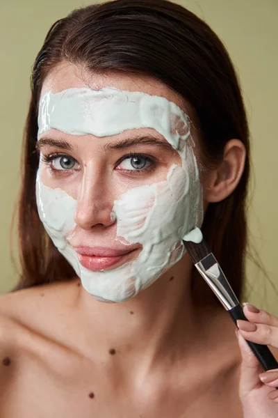 Chica con expresión facial complacido y máscara de arcilla en la cara conseguir tratamientos de belleza —  Fotos de Stock