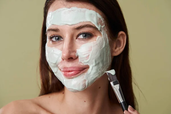 Mujer alegre aplicando su mascarilla de barro mientras posa con los hombros desnudos — Foto de Stock