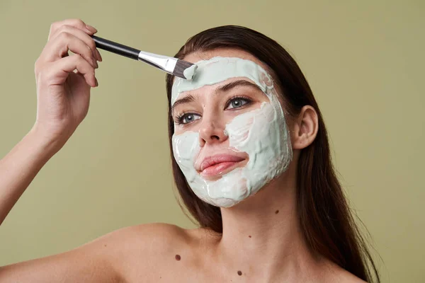 Brunette berambut muda menerapkan masker tanah liat dengan sikat kosmetik — Stok Foto