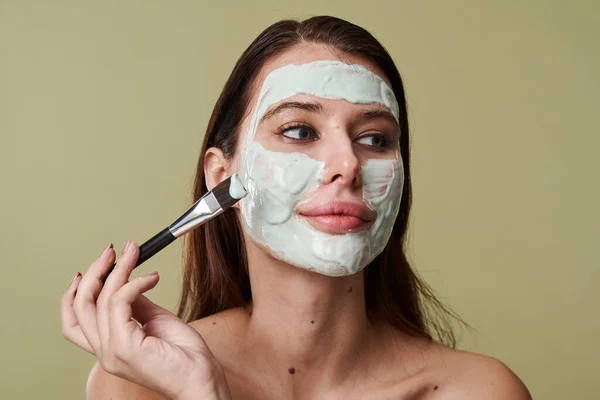 Mujer joven aplicando máscara natural de arcilla con cepillo cosmético — Foto de Stock