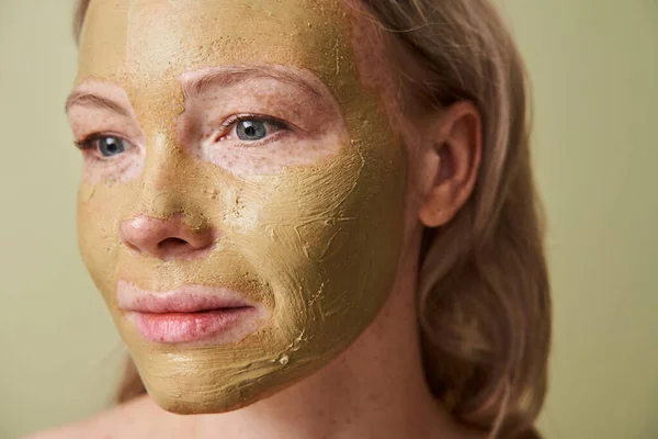Gadis menarik dengan masker tanah liat di wajah berpaling terisolasi atas latar belakang hijau — Stok Foto