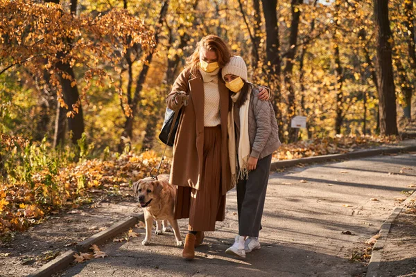 Moeder en dochter dragen beschermende maskers die met elkaar verbonden zijn tijdens het lopen — Stockfoto