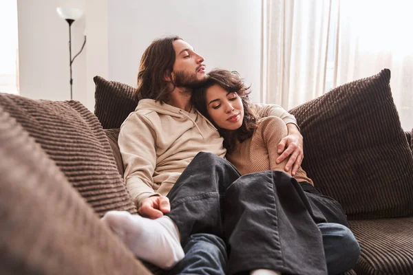 Пара улыбается и обнимается, лежа дома на диване — стоковое фото