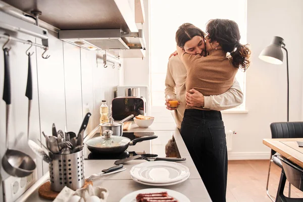 Par omfamnar när de står i köket hemma tillsammans — Stockfoto