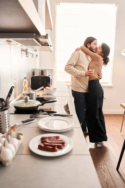 Pár objímání, zatímco stojí v kuchyni doma spolu — Stock fotografie