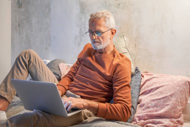 Çekici kıdemli gri saçlı adam akşamları dizüstü bilgisayar kullanıyor.