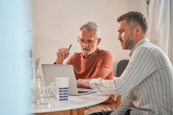 Adult son and senior father using laptop at home while discussing something — Stock Photo, Image