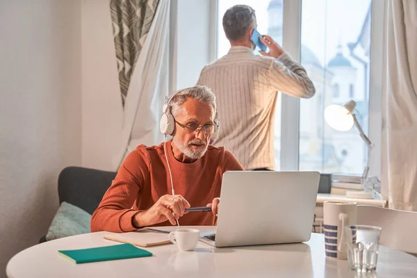 Adult man talking via smartphone while his father having video call at the laptop — Stock Photo, Image