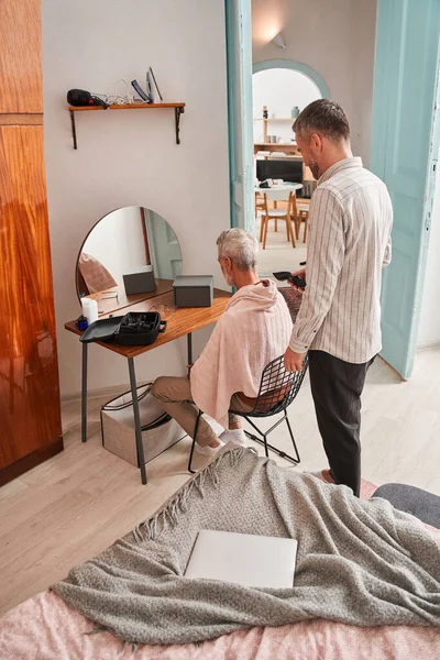 Adult son making haircut for his father at home with haircut machine