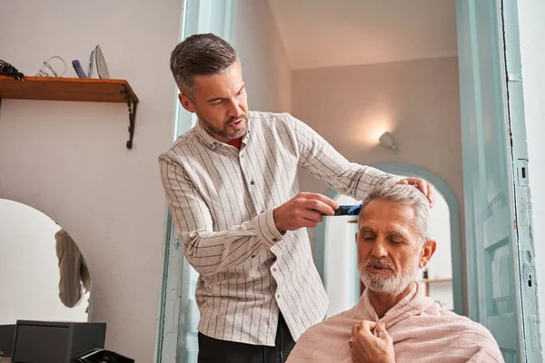 Middelbare leeftijd zoon knippen haar naar zijn pensioen vader alleen thuis tijdens het chatten — Stockfoto