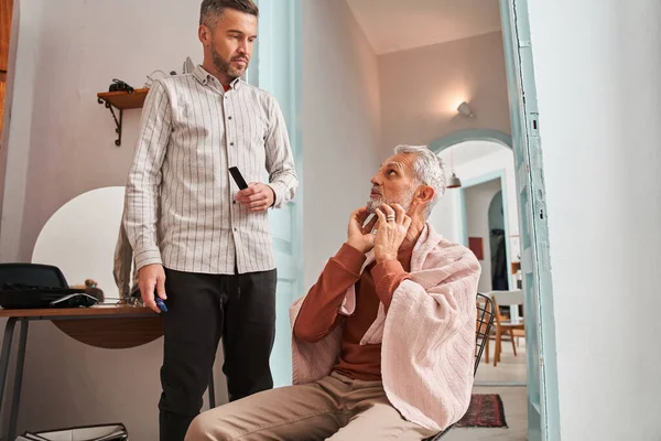 Старший чоловік показує своєму дорослому синові яку бороду і стрижку він хоче — стокове фото