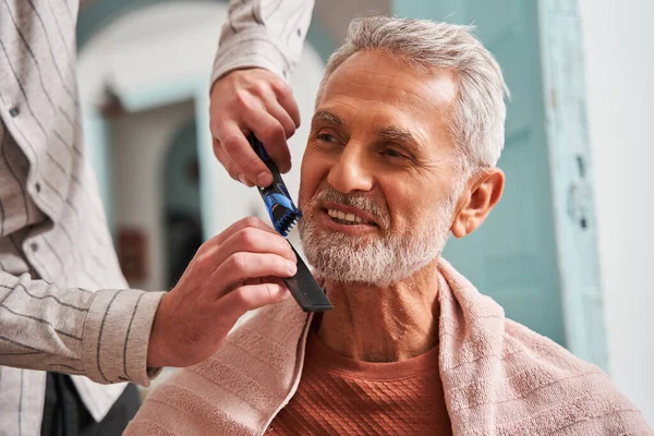 Старший чоловік почувається щасливим, коли його син допомагає йому перерізати бороду під час пандемії — стокове фото