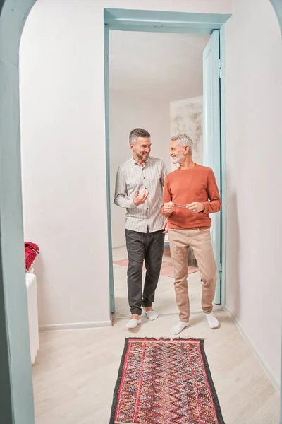 Senior man en zijn zoon staan bij de ingang van de deur en lachen terwijl ze met elkaar kletsen — Stockfoto