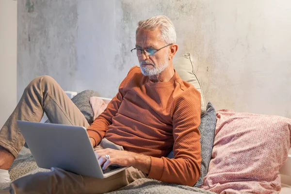 Çekici kıdemli gri saçlı adam akşamları dizüstü bilgisayar kullanıyor. — Stok fotoğraf