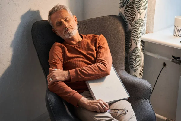 Man slaapt in de gezellige fauteuil met boek over zijn taille — Stockfoto
