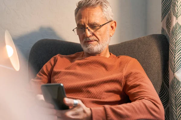 Volwassen man communiceren via mobiele telefoon in zijn kamer terwijl zitten aan de fauteuil — Stockfoto