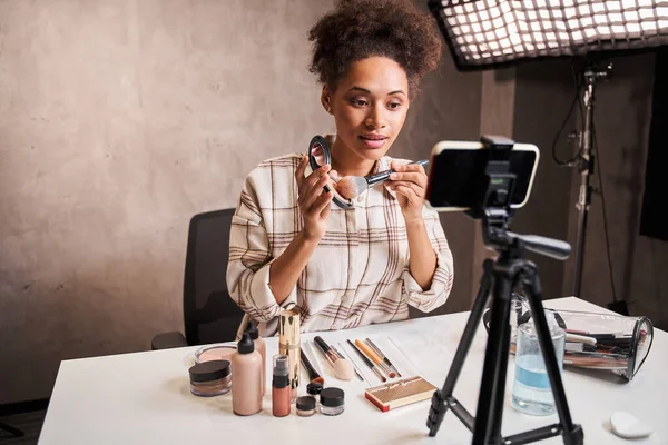 Multiracial woman picks up blush on the brush while broadcasting make up tutorial — Stock Photo, Image