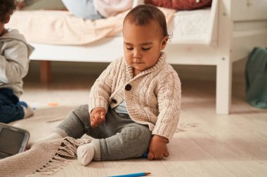 Çok ırklı bir çocuk yerde oturuyor ve ağabeyi ve sevgili annesinin yanında oynuyor.