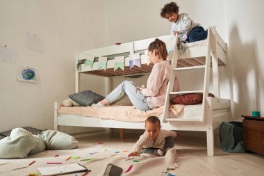 Şefkatli beyaz anne ve tatlı küçük çocuklar yatakta birlikte oynuyorlar.