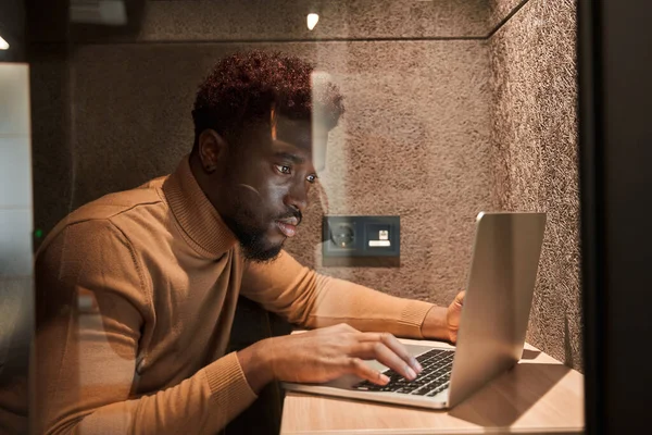 Bello giovane seduto a tavola con computer portatile in poco spazio mentre si lavora — Foto Stock