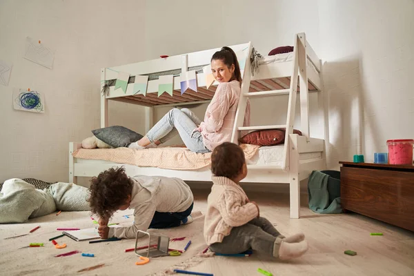Mujer relajándose con sus dos hijos en el dormitorio durante el juego en la mañana —  Fotos de Stock