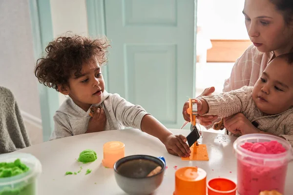 Niños multiraciales disfrutando del juego mientras se sientan a la mesa con su madre caucásica —  Fotos de Stock