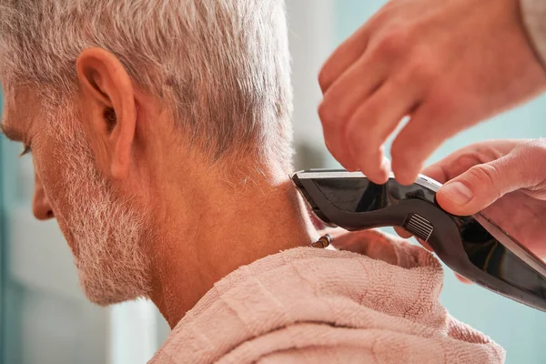 Сын бреет голову своего отца на пенсии, помогая стричься. — стоковое фото