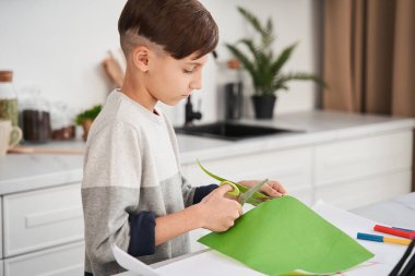 Uygulamayı hazırlarken elinde makasla kağıt kesen konsantre küçük çocuk.
