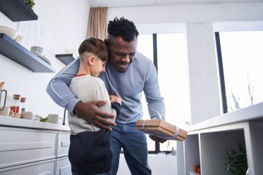 Anaokulu çocuğu, mutfakta çok kültürlü babasına bayram hediyesi sunuyor.