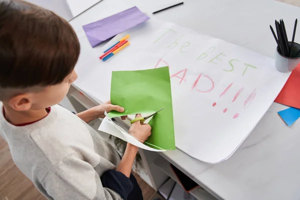 Kafkas çocuk renkli kağıt ve makas tutuyor ve yaratıcı hediyeyi hazırlarken kesiyor. — Stok fotoğraf