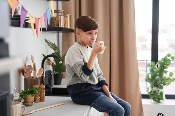 Niño tranquilo sentado en el camarero y bebiendo té mientras espera a su padre — Foto de Stock