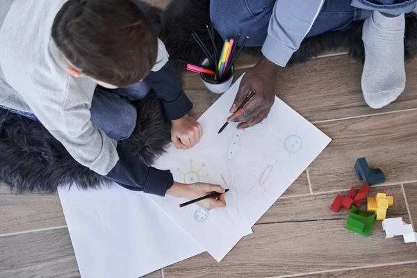 Çok ırklı bir baba, yerde dikkatle resim çizerken oğluna bir şey anlatıyor. — Stok fotoğraf