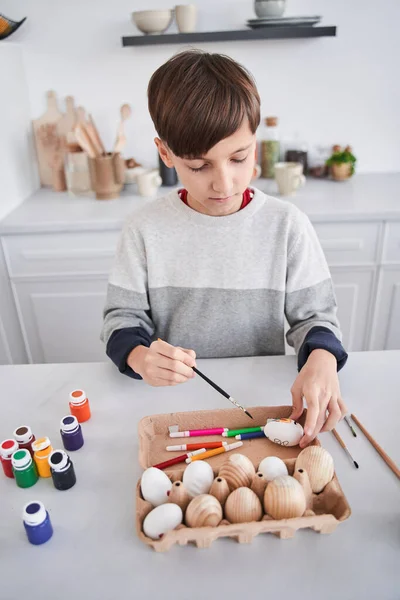 Keçeli kalemle çizerken tahta masada farklı paskalya süsleri yapan bir çocuk. — Stok fotoğraf