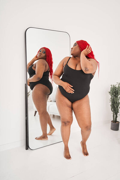 Beautiful young multiracial woman standing in front of the mirror and looking at her reflection