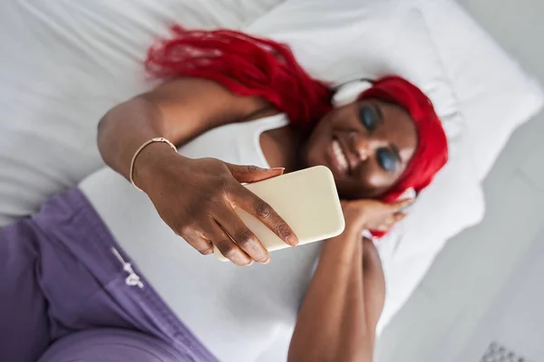 音楽を聴きながらベッドの上に寝そべっている幸せな若い女性 — ストック写真