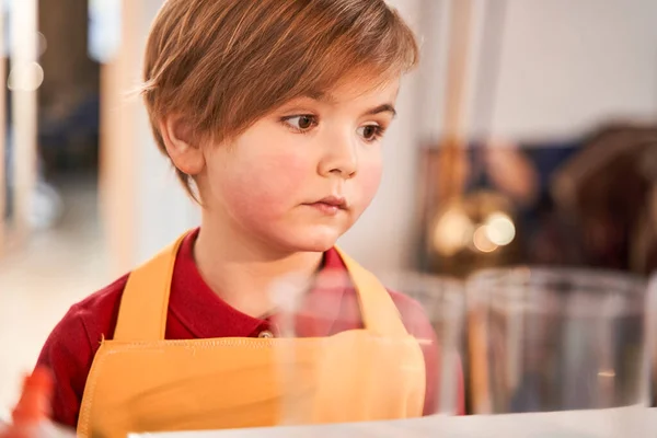 Serious cute child standing at the art studio and looking at something while preparing drawing — Stock Photo, Image