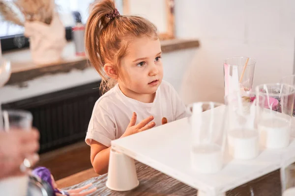 Niña mirando a alguien con atención mientras está de pie en la mesa con pinturas —  Fotos de Stock