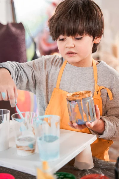 Pensive brunette boy standing comfortably at the table and drawing at the canvas — Stock Photo, Image