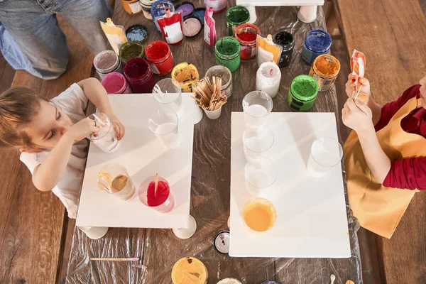 Roztomilé předškolní děti stojící u stolu a kreslení na plátno s barvami různých barev — Stock fotografie