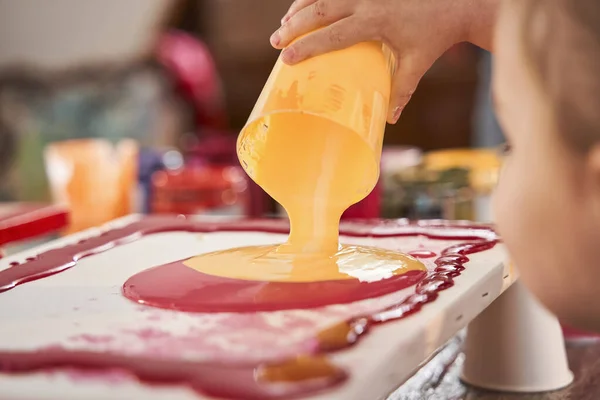 Boy pouring fresh orange paints into the canvas while creating his own abstract masterpiece — Stock Photo, Image