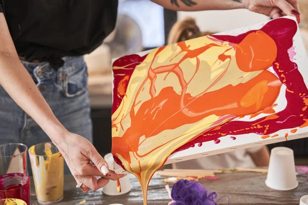 Artista mujer sosteniendo lienzo con pinturas frescas que fluyen de ella mientras dibuja en su estudio de arte —  Fotos de Stock