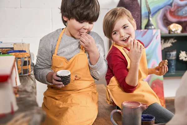 Happy kids sitting at the table and eating cookie during the break after art lesson — Stock Photo, Image
