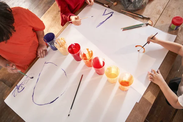 Çocuklar resim dersinde vakit geçirirken fırça ve akrilik boyalarla kağıt çiziyorlar. — Stok fotoğraf