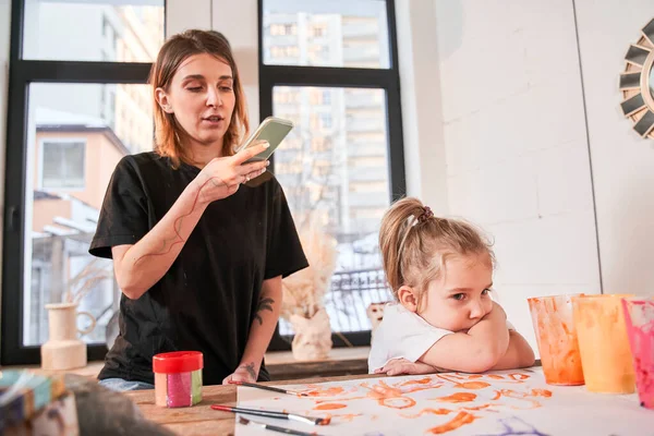 Žena učitel drží smartphone a střílet kreslení, zatímco holčička demonstrující negativní emoce — Stock fotografie