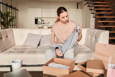 Kanepede oturan ve paketleri açarken kıyafetlerini inceleyen yapay bacaklı bir kadın.