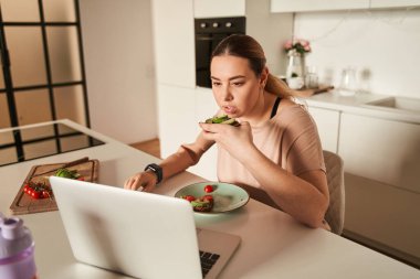 Yapay bacaklı hoş bir kadın mutfakta otururken kahvaltısını yiyor.